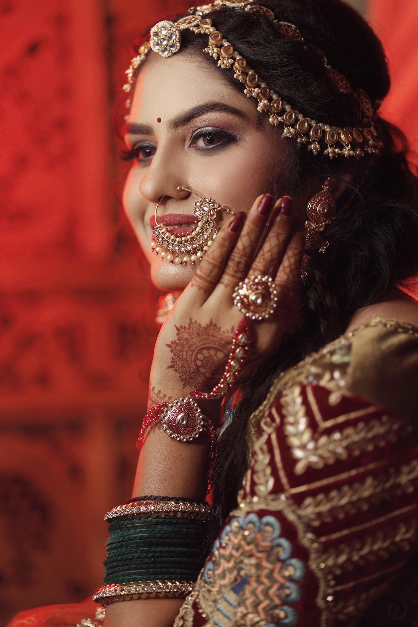 A young Indian woman adorned in traditional clothing with henna tattoos and jewelry, smiling gracefully.