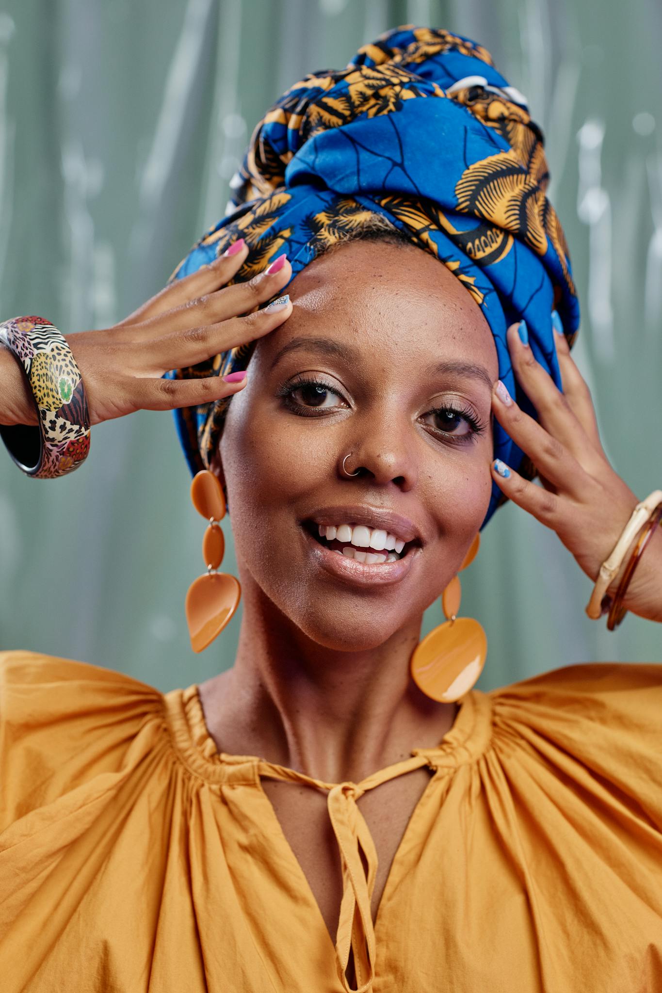 Portrait of a joyful woman wearing a colorful headwrap, earrings, and bracelets.