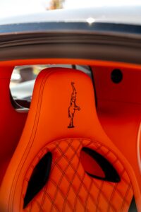 Close-up of luxurious orange car seat with detailed stitching and logo.