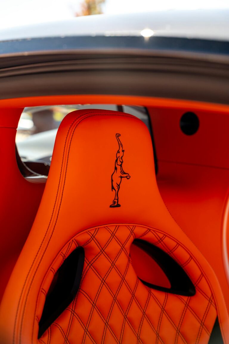 Close-up of luxurious orange car seat with detailed stitching and logo.